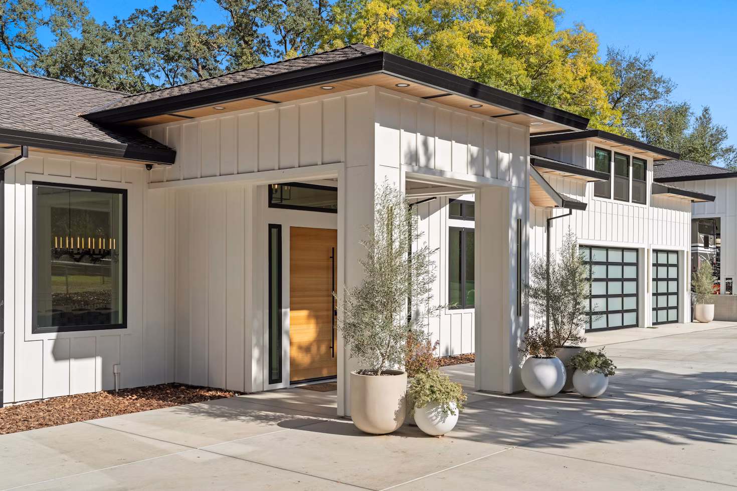 Contemporary white residential property with a wood entry and olive trees